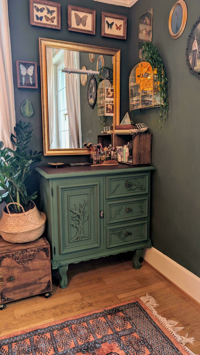 Decorated cozy home corner with vintage green cabinet, large mirror, butterfly wall art, and indoor plants on wooden floor.