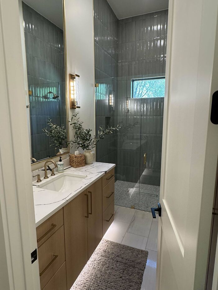Modern bathroom corner with sleek wood vanity, marble countertop, glass shower, and decorative plant showcasing home decorating pride.