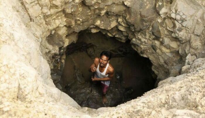 Man standing inside a deep rocky hole, illustrating a chaotic good morally grey act in an unusual setting.