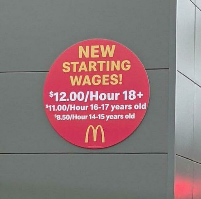 Red circular sign at McDonald's showing new starting wages for different age groups indicating economic changes.