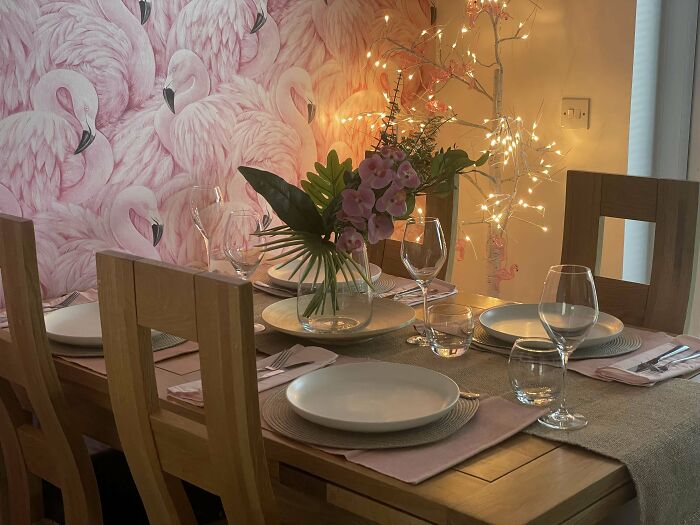 Cozy dining area with wooden chairs, flamingo wall art, floral centerpiece, and warm decorative lighting in home corners.