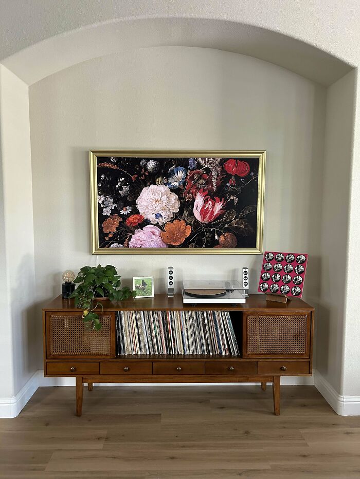 Mid-century home decor corner featuring a record player, vinyl collection, plant, and floral artwork on neutral walls.