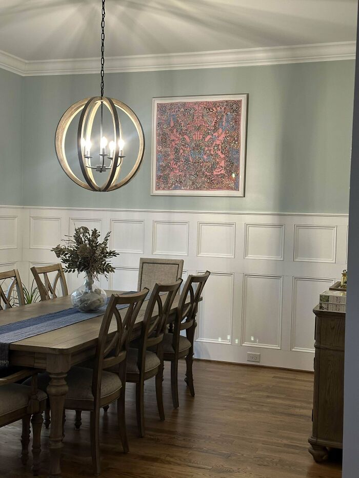 Dining room corner with wood furniture, decorative chandelier, artwork, and wall paneling showcasing home decorating pride.