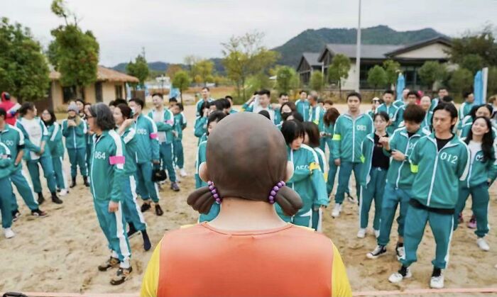 Contestants in green tracksuits facing a bald man with pigtails, referencing a point of no return in a game scenario.