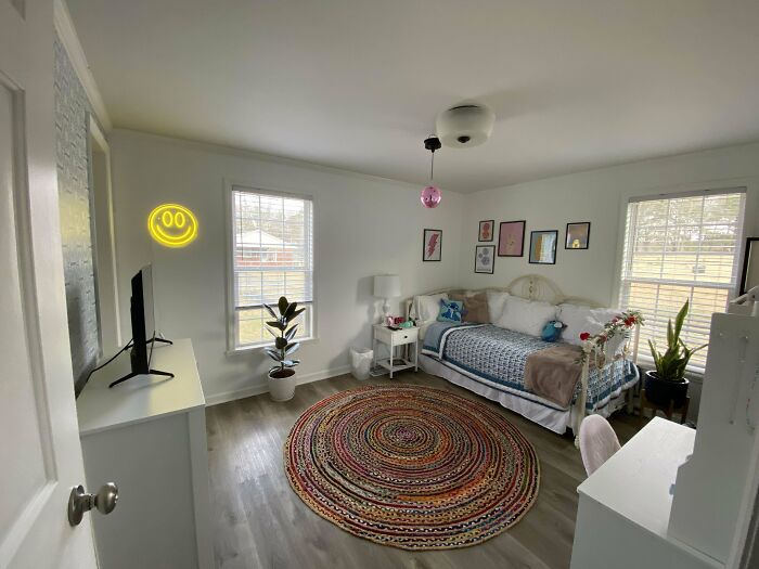 Cozy decorated home corner with a bed, colorful circular rug, plants, and framed wall art showcasing proud decorating.
