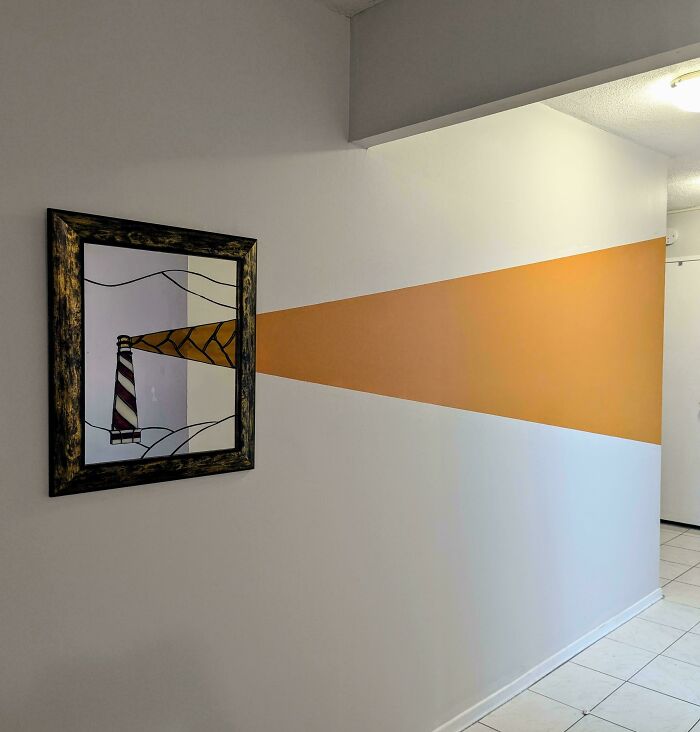 Wall corner decorated with a lighthouse painting and an orange beam, showcasing creative home decorating pride.