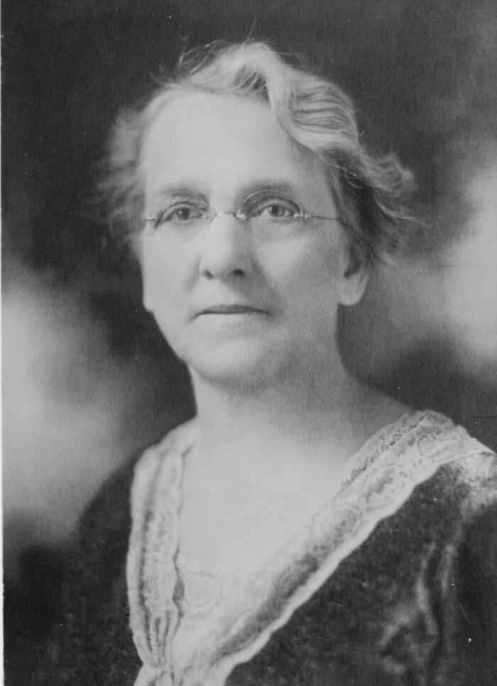 Black and white portrait of a remarkable woman scientist wearing glasses and a lace-trimmed blouse in a formal setting