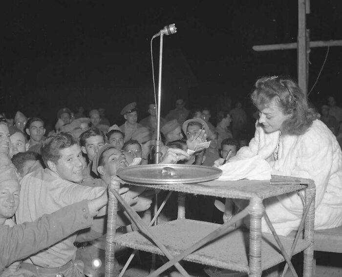Rare WWII photo of soldiers eagerly reaching to get an autograph from a woman in a white fur coat at a wartime event.