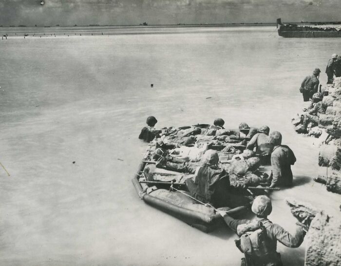 Soldiers navigating a makeshift raft near shore during a rare WWII moment captured in black and white.