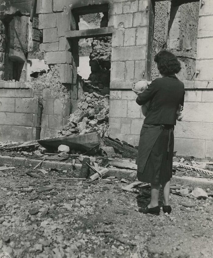 Woman holding a baby standing in front of a destroyed building in a rare WWII photo showing war devastation.