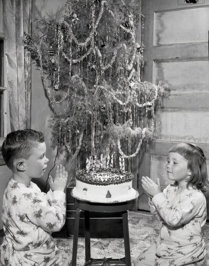 Two children in pajamas praying by a birthday cake under a decorated tree in 1950s Florida everyday life.