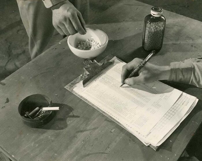 Rare WWII photo showing two soldiers handling medication and documenting on a clipboard during wartime.