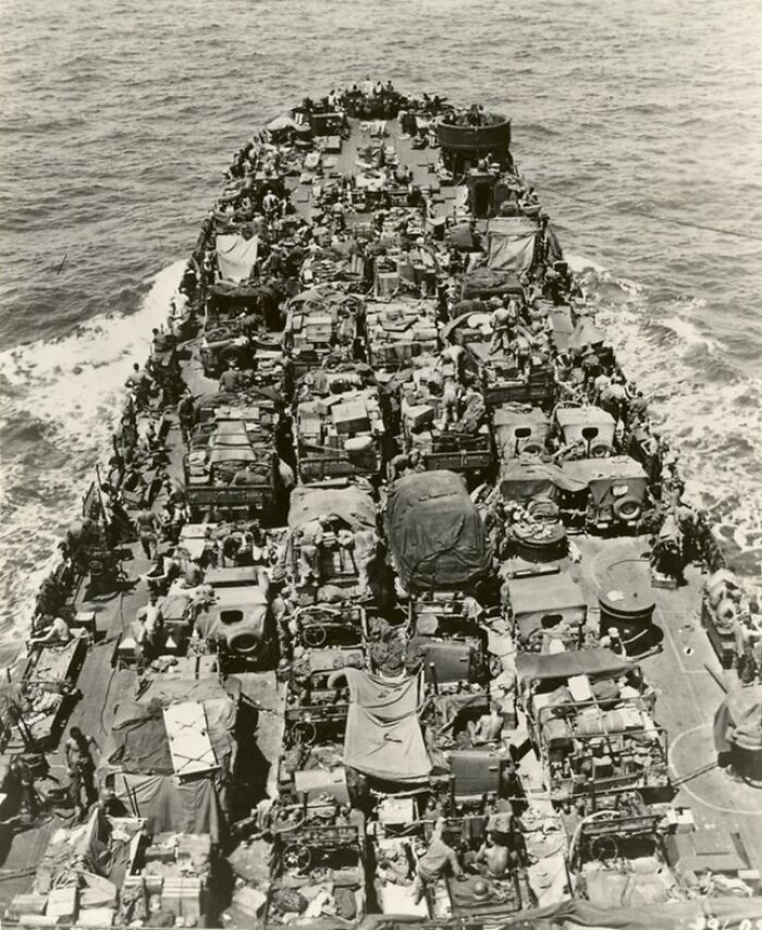 WWII rare photo showing a heavily loaded military ship transporting vehicles and troops across the ocean during wartime.