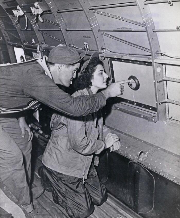 Two WWII soldiers inside an aircraft, one pointing outside through a small window, rare WWII photos glimpse.