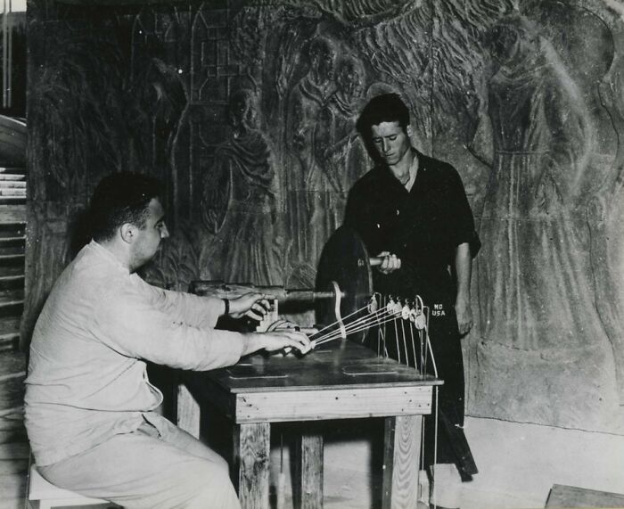 Two men examining or restoring ancient artifacts in a workshop, rare WWII photos capturing historical preservation efforts.