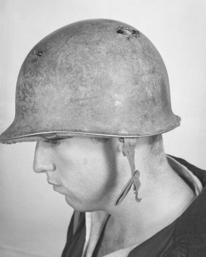 Close-up of a soldier wearing a battle-damaged helmet in a rare WWII photo from an unseen collection.