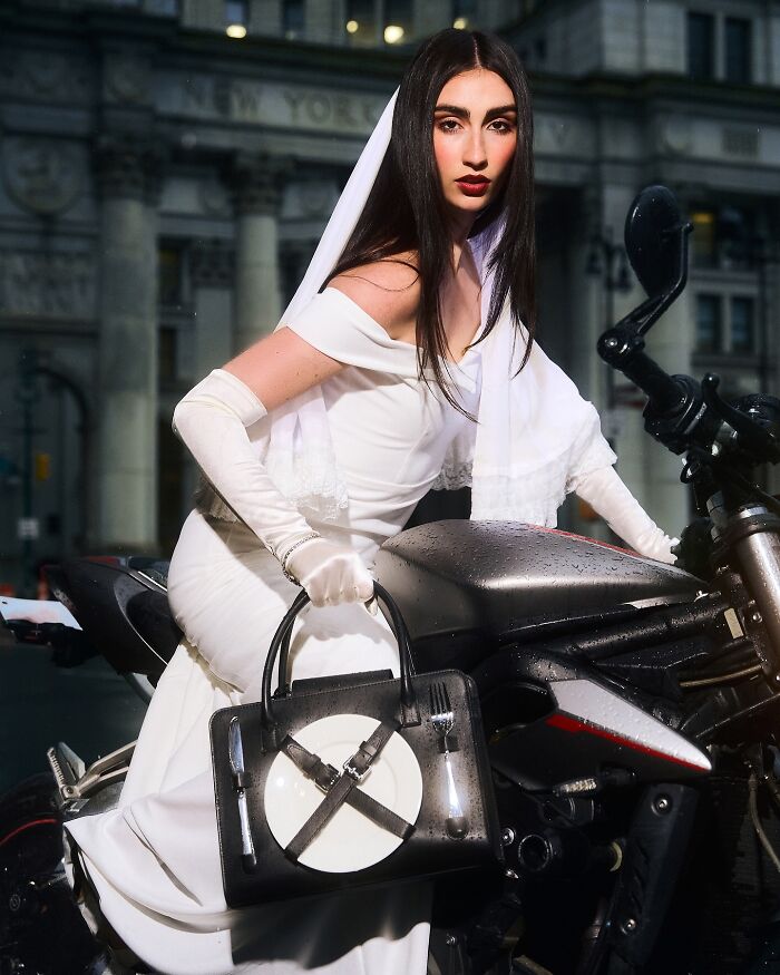 Woman in a white dress holding an unusual accessory handbag featuring a plate and cutlery, blending everyday objects with fashion.