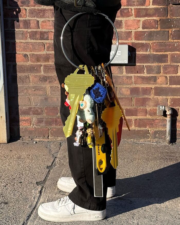 Person wearing white sneakers and black pants holding a large keyring with unusual fashion accessories by Nik Bentel.