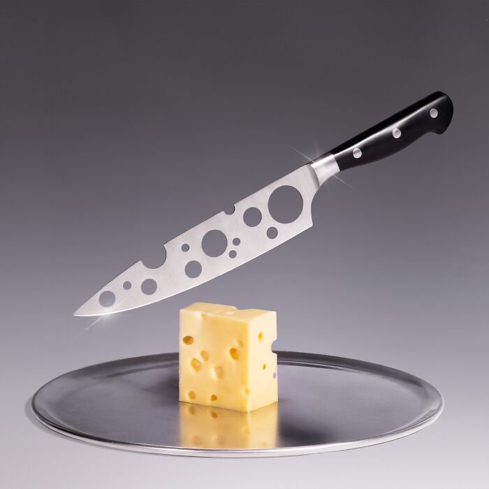 Cheese knife with unusual holes floating above a block of Swiss cheese on a metal tray, showcasing unusual accessories.
