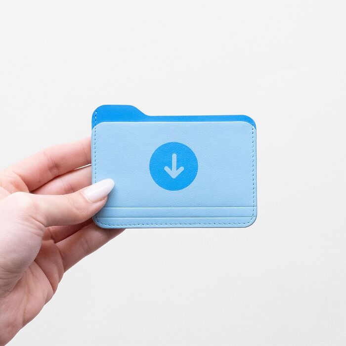 Hand holding a blue cardholder shaped like a file folder, an unusual accessory blending everyday objects with fashion.