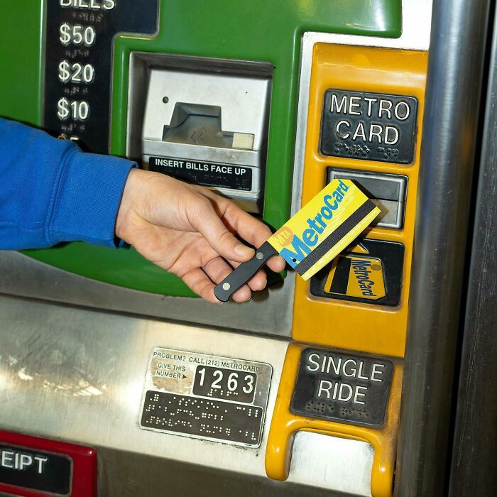 Hand holding MetroCard attached to a knife accessory at a subway vending machine blending fashion with everyday objects.