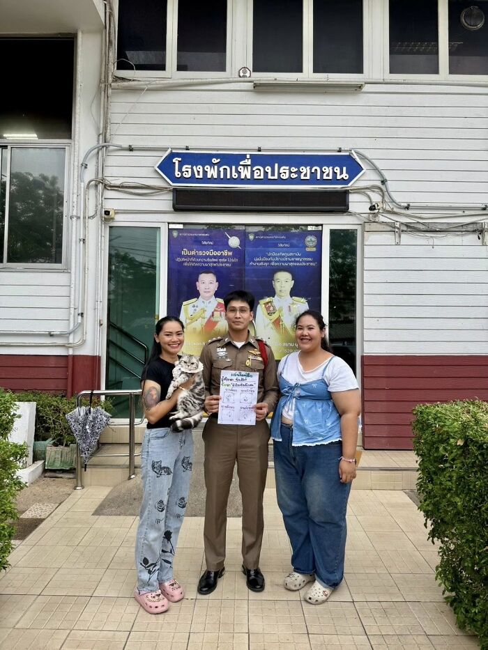 Police officer and two women stand outside a station holding a cat and a mugshot related to cat arrest viral photo.