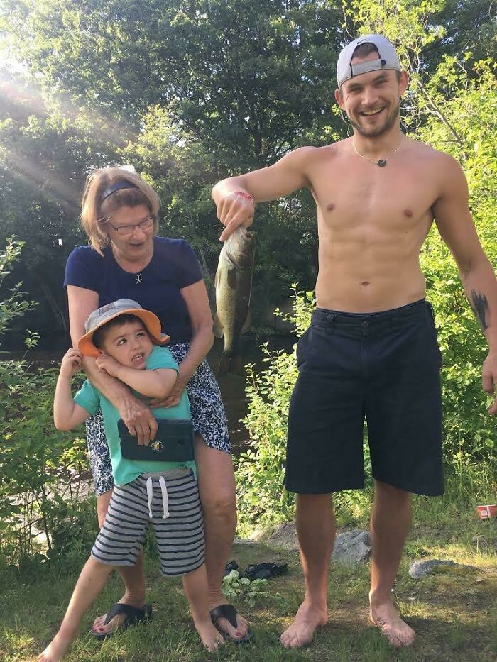 Family on vacation by river with a man holding a fish, capturing funny vacation pics with kids and adults outdoors.