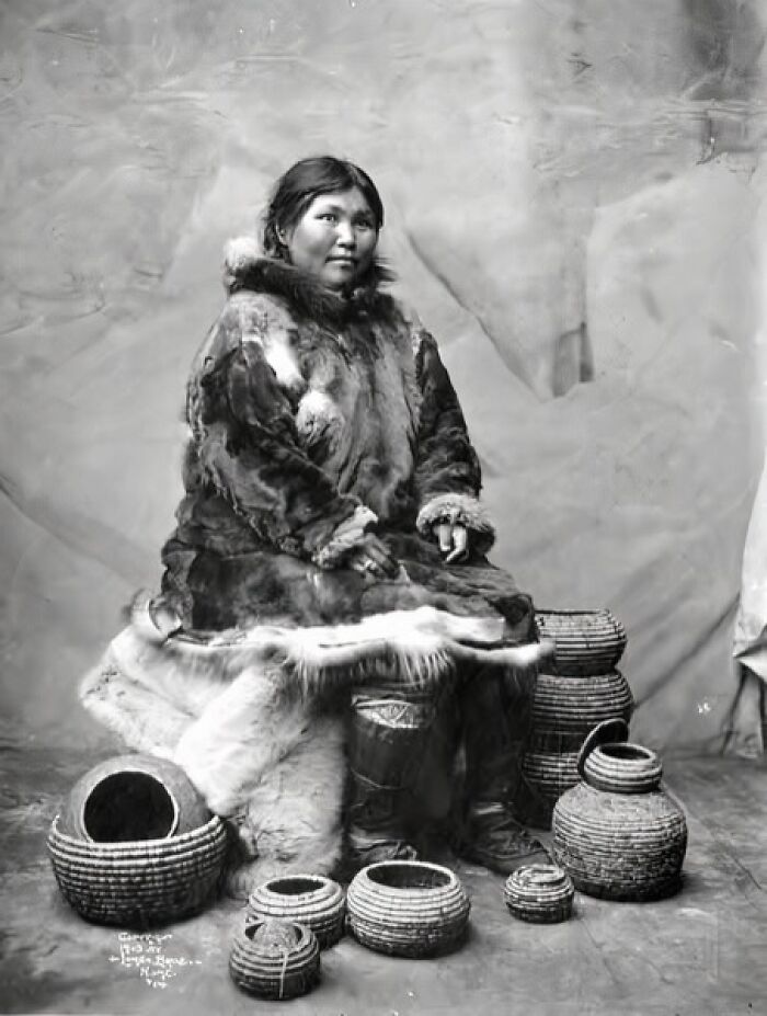Inuit woman dressed in traditional fur clothing sitting surrounded by historic woven baskets, capturing Inuit spirit.