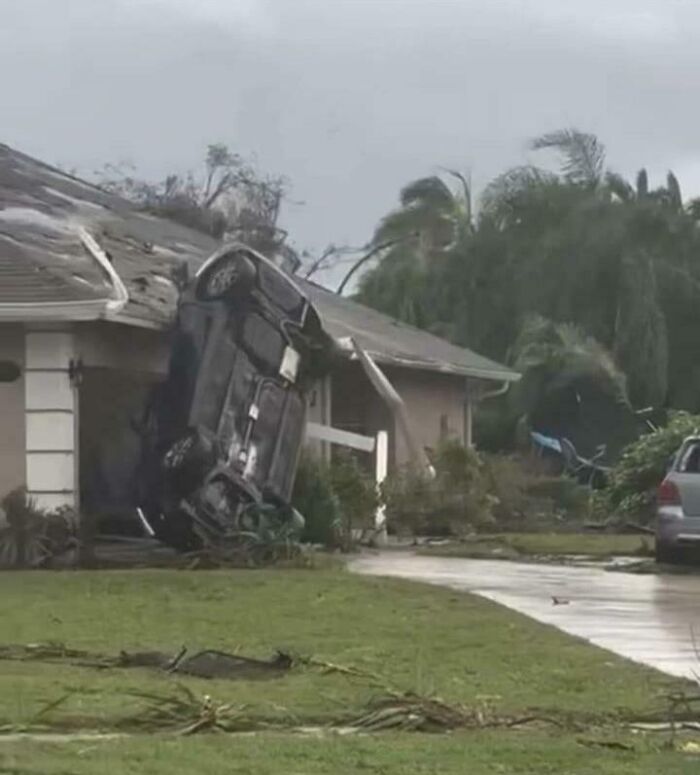 Car flipped onto its side against a house after severe storm showing wild power of Mother Nature damage.