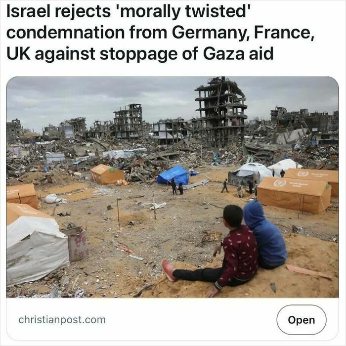 Children sit amid rubble and tents in a destroyed area, illustrating harsh realities in headlines that pass for satire but are true.