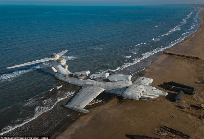 An extremely large, derelict plane washed ashore on a beach, presenting a scary and eerie scene by the ocean.