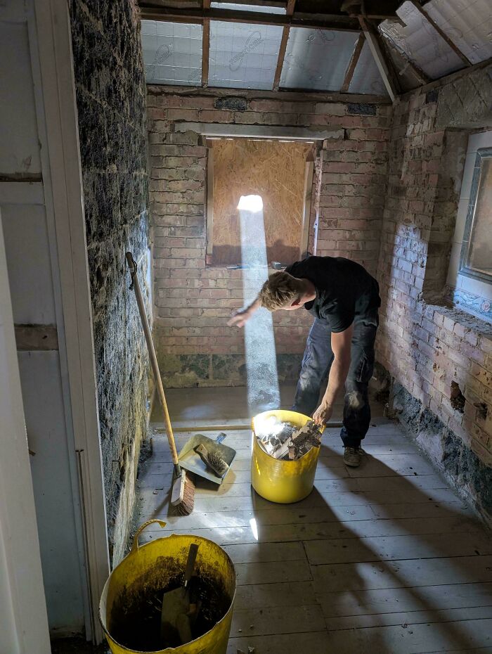 Man cleaning debris in a sunlit rustic room, creating an accidental renaissance photo with a beam of light.