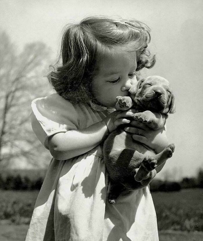 Young girl holding and kissing a puppy in a candid glimpse into the past, captured in a black and white photo.