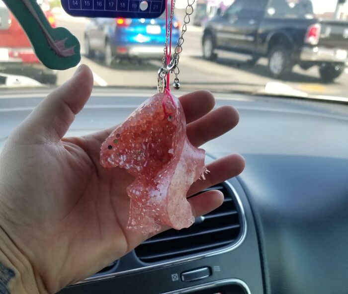Mano sosteniendo adorno derretido dentro de un coche, mostrando daños por altas temperaturas de olas de calor veraniegas.