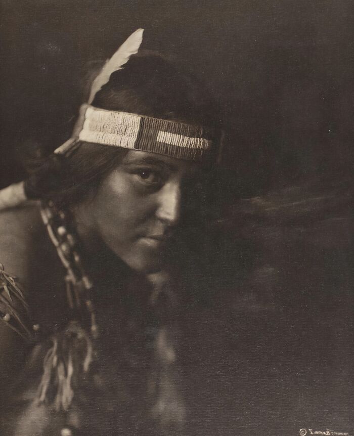 Portrait of a Native tribesperson wearing traditional attire, captured with strength and dignity in early 1900s photography.
