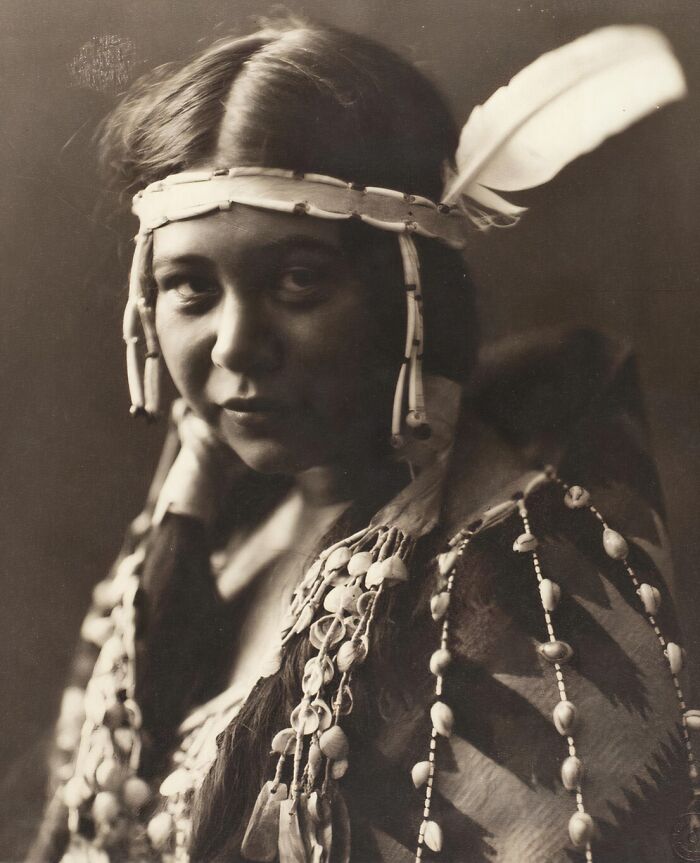 Vintage portrait of a Native American woman wearing traditional attire with beadwork and a feathered headband, showcasing strength.