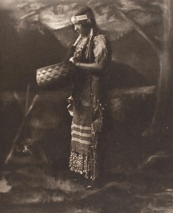 Native tribes member in traditional dress holding a patterned basket, showcasing the strength of native tribes in the 1900s.