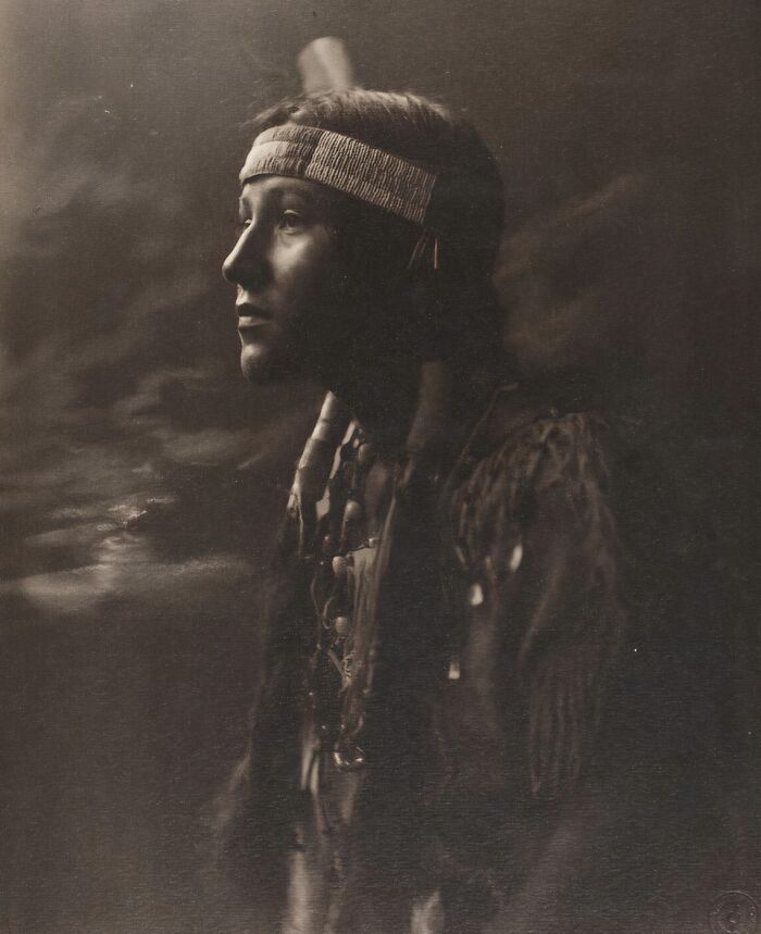 Native tribes member in traditional attire and headband, captured in a powerful 1900s photograph showing strength and heritage.