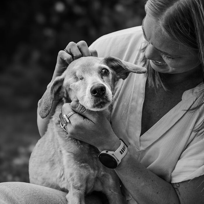 Woman gently holding and comforting one-eyed dog, capturing touching final moments between pets and their humans in black and white.