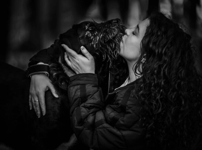 Woman with curly hair holding and kissing her dog, capturing touching final moments between pets and their humans.