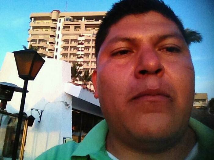 Man taking a vacation selfie with a building and street lamp in the background, a funny vacation pic moment.