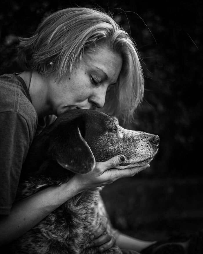 Woman tenderly holding and kissing her elderly dog, capturing touching final moments between pets and their humans in black and white.