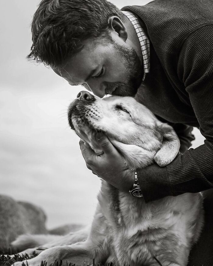 Man tenderly kissing his dog, capturing touching final moments between pets and their humans in black and white.