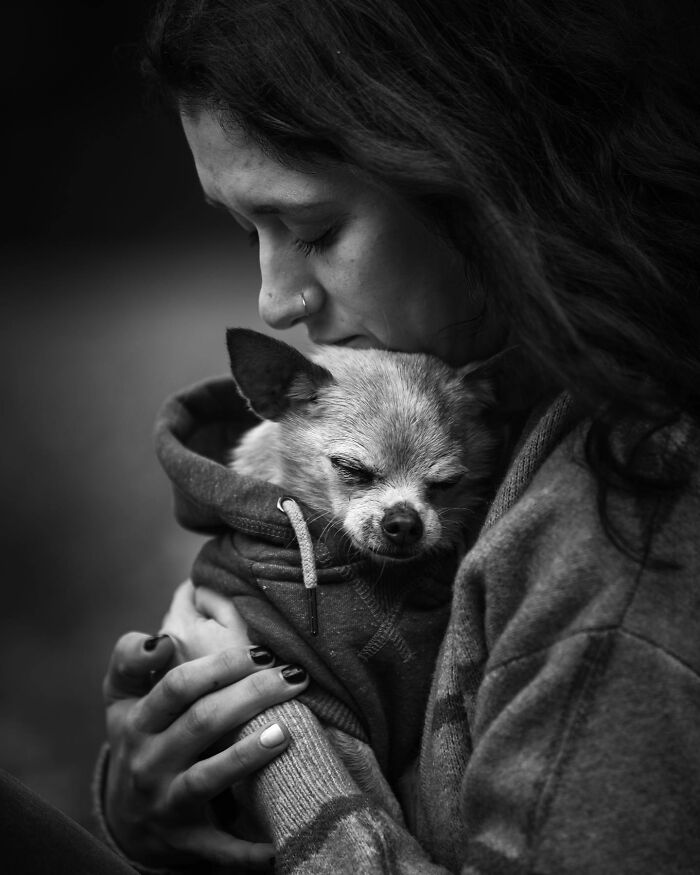 Woman gently holding and comforting her small dog, capturing touching final moments between pets and their humans in black and white.