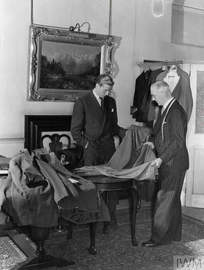 Two men examining fabric in a tailor’s shop, illustrating British women keeping style during WWII restrictions.