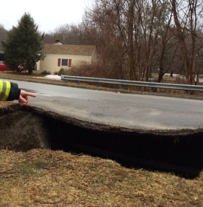 Large sinkhole caused by nature undermining the road, showcasing wild Mother Nature doing things on its own terms.