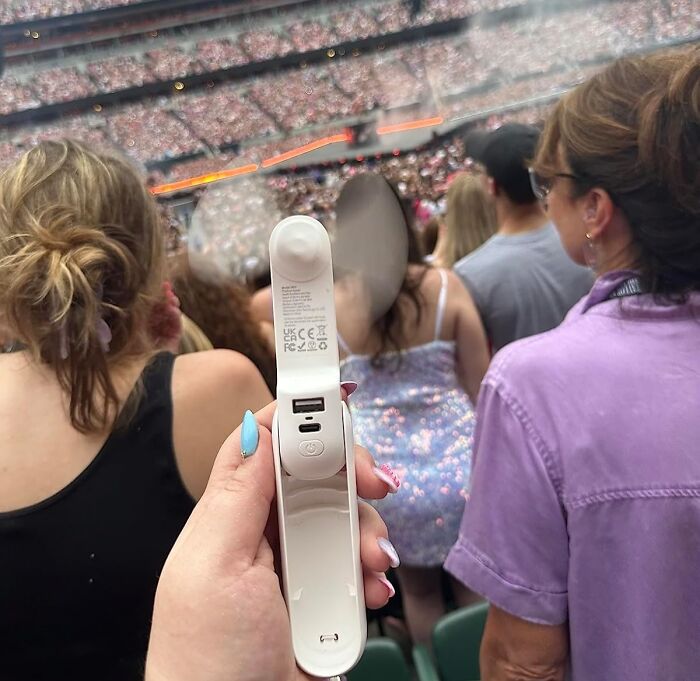 Hand holding a portable mini fan at crowded outdoor event, demonstrating heatwave hacks to stay cool during summer.