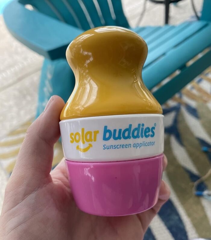 Hand holding a Solar Buddies sunscreen applicator with a yellow top and pink base on a patio chair.