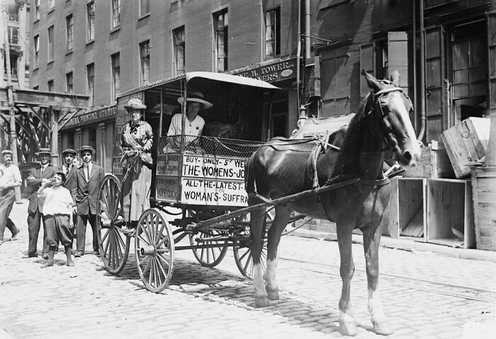 Horse-drawn wagon with women promoting suffrage newspapers on a city street during the 20th century suffrage era.