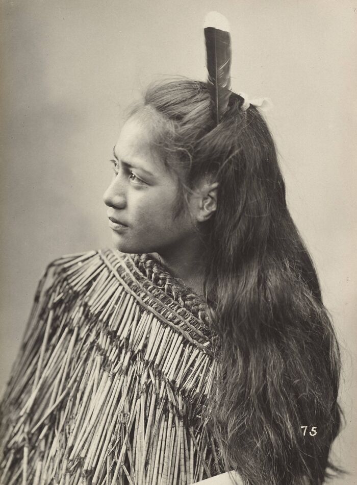 Portrait of a young Māori woman from a century ago wearing traditional clothing and a feather in her hair.
